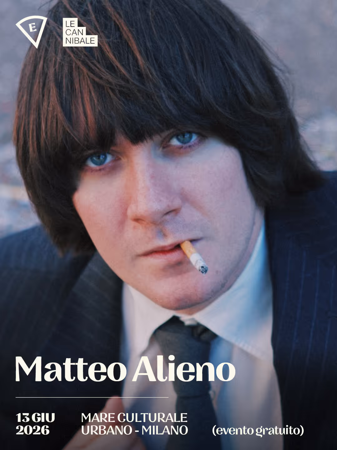 Portrait of a man with blue eyes and dark hair smoking a cigarette, wearing suit and tie.