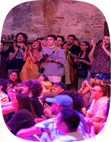 Audience watching a performance in a dimly lit venue with exposed brick walls and purple lighting.